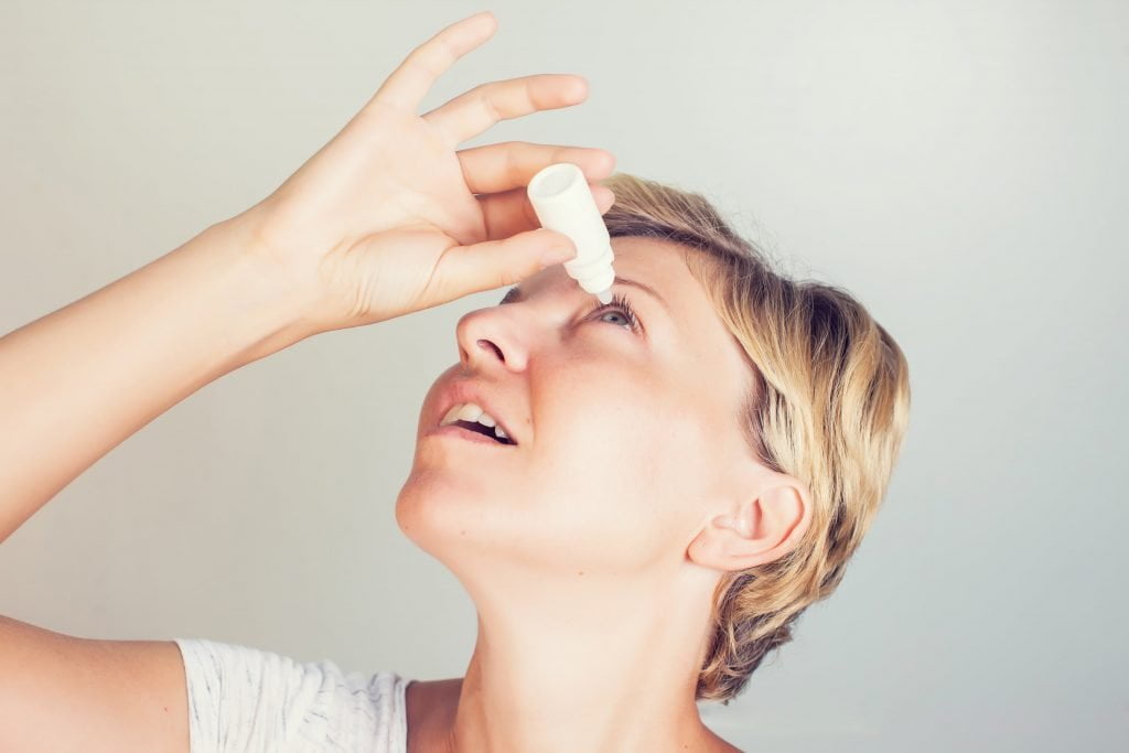 woman putting in eye drops to treat pink eye