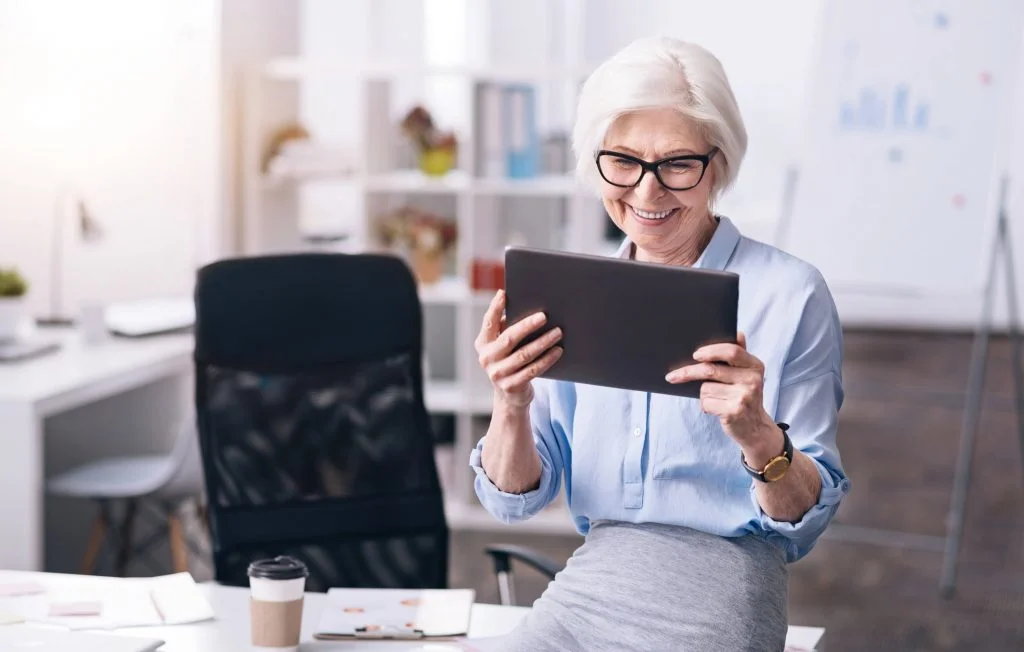 older woman wearing glasses looking at a tablet in office 