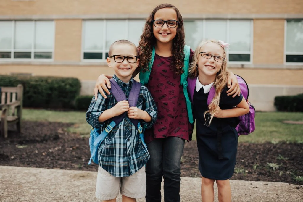 3 kids wearing glasses in front of school 