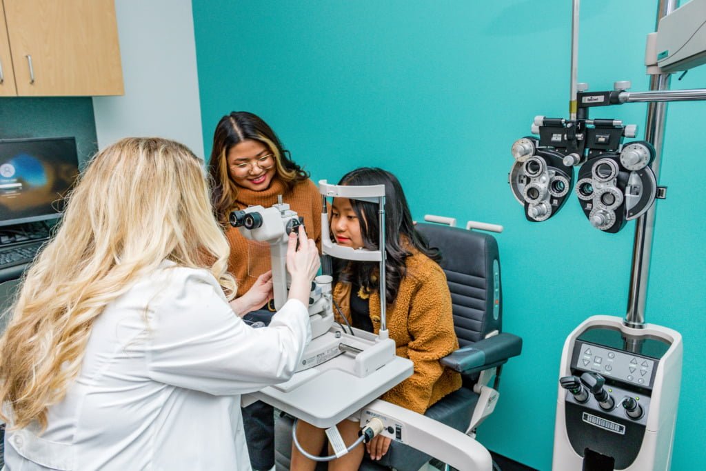 A child sitting behind a slit lamp during a kids eye exam with an optometrist. 